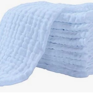 May include: A stack of 10 soft, white, muslin cloths with a textured waffle weave. The cloths are folded and stacked neatly.