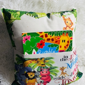 May include: A white pillow with a green jungle print and a pocket on the front. The pocket holds a book with a giraffe and the words "Rumble in the Jungle" on the cover. The pillow also has the words "Jungle in the Night reads" on the front.