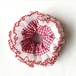 May include: Red and white gingham hair scrunchie with white ruffled trim and red stitching.