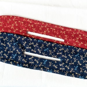 May include: Two fabric hair ties with a dragonfly pattern. The top hair tie is red with white dragonflies. The bottom hair tie is navy blue with white and blue dragonflies.