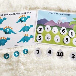 Puede incluir: Un conjunto de dos juegos educativos para ni&ntilde;os con dinosaurios y n&uacute;meros. El primer juego tiene dinosaurios azules con n&uacute;meros en la espalda. El segundo juego tiene huevos blancos con n&uacute;meros en ellos. Los juegos est&aacute;n dise&ntilde;ados para ayudar a los ni&ntilde;os a aprender a contar y a emparejar n&uacute;meros.