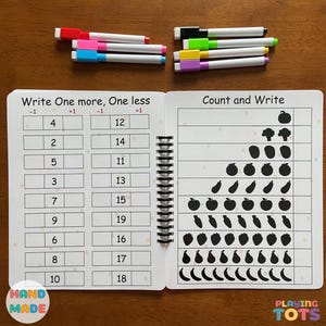 May include: A spiral-bound educational workbook with number exercises and fruit and vegetable counting activities. Includes colorful markers in red, pink, blue, green, yellow, and purple. The workbook has the text "Write One more, One less" and "Count and Write".