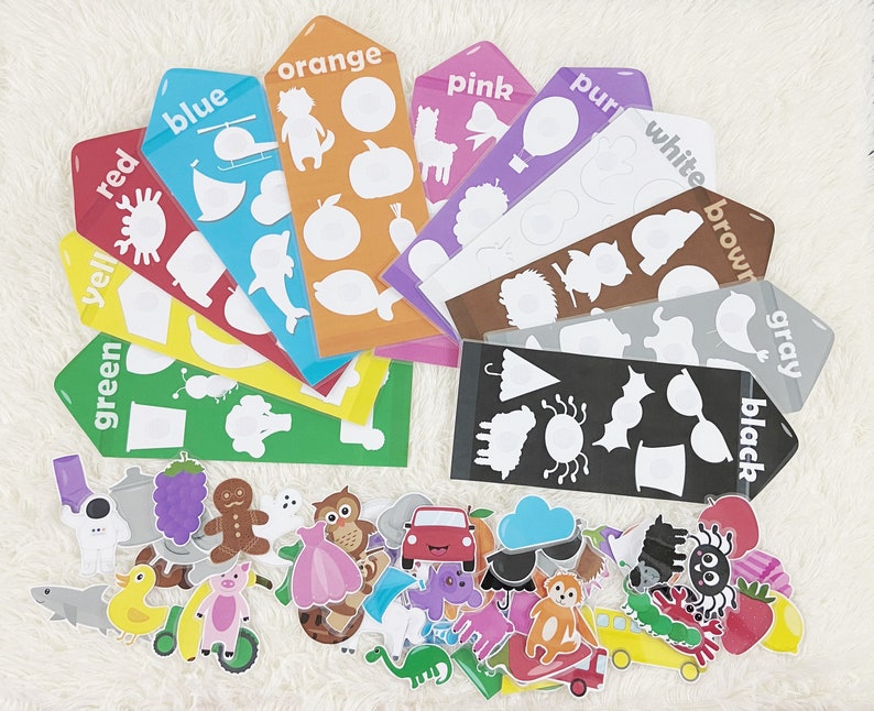 May include: A set of colorful learning cards with matching picture pieces. The cards feature different colors, including red, orange, yellow, green, blue, purple, white, brown, gray, and black. Each card has a silhouette of an object, and the matching picture pieces can be placed on top of the silhouette.