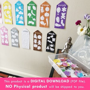 May include: A set of 12 color cards with white outlines of various objects. Each card has a color name at the top and a white circle in the center. The cards are displayed on a white wall. A clear plastic storage box with a variety of colorful stickers is in the foreground.