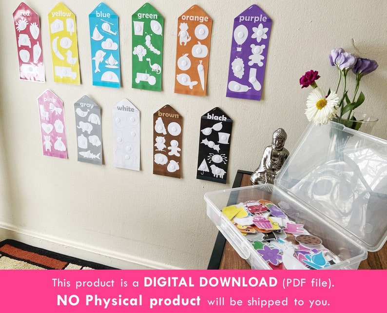 May include: A set of 12 color cards with white outlines of various objects. Each card has a color name at the top and a white circle in the center. The cards are displayed on a white wall. A clear plastic storage box with a variety of colorful stickers is in the foreground.
