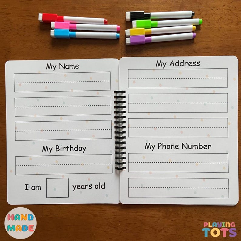 May include: Open spiral-bound activity book with fill-in-the-blank sections for name, address, birthday, and phone number. The book is open on a wooden surface with colorful markers in red, pink, blue, black, green, yellow, and purple.