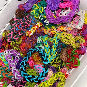 May include: A collection of colorful rubber band bracelets in a white container, featuring various braided patterns and solid colors including purple, blue, green, pink, and yellow. The text "Single loop" is printed in black in the upper left corner.