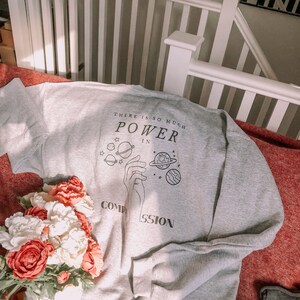 May include: Gray sweatshirt with a graphic print of a hand holding planets and the text "There is so much power in compassion".