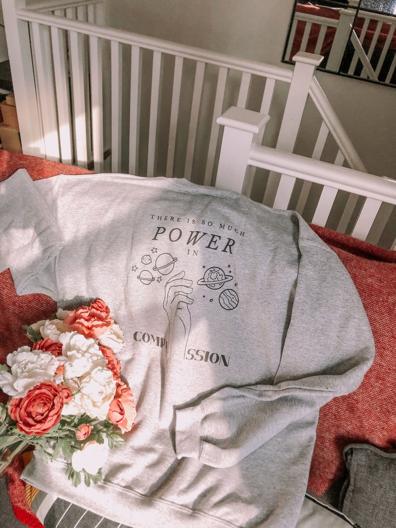 May include: Gray sweatshirt with a graphic print of a hand holding planets and the text "There is so much power in compassion".