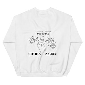 May include: White sweatshirt with a black graphic design featuring a hand holding planets and the text "There is so much power in compassion."