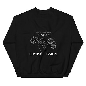 May include: Black sweatshirt with a white graphic design featuring a hand holding planets and the text "There is so much power in compassion."
