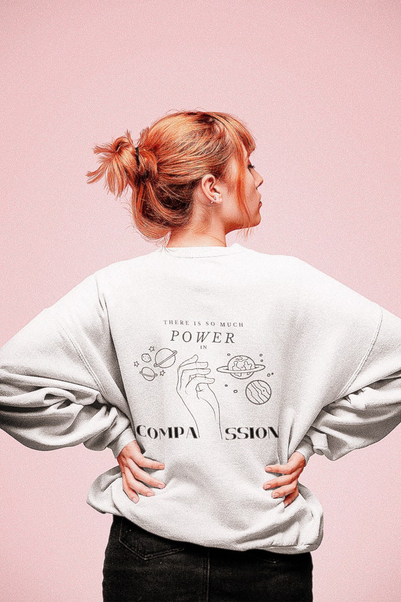 May include: A white sweatshirt with a graphic print of a hand holding planets and the text "There is so much power in compassion".