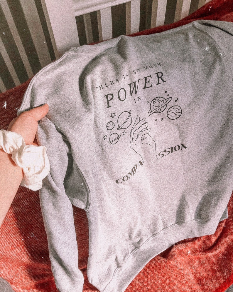 May include: Gray sweatshirt with a graphic print of a hand holding planets and the text "There is so much power in compassion".