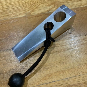 May include: A silver metal wedge with two holes and a black bungee cord with a black ball on the end.