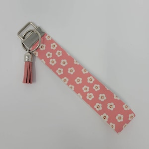 May include: A pink key chain with a white tassel and a pattern of white smiley faces on a pink background.