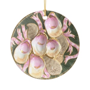 May include: A round, decorative ornament with a gold hanging string. The ornament features a dark green background with pink and gold accents. The design includes pink, white, and gold floral elements, creating a delicate and elegant aesthetic.