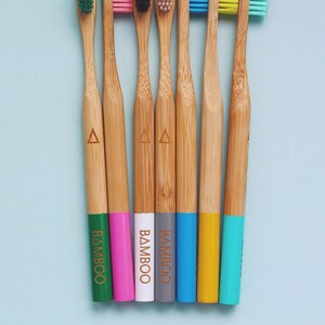 May include: Seven bamboo toothbrushes with colorful bristles and handles. The handles are painted in different colors, including green, pink, white, gray, blue, yellow, and turquoise. The word "BAMBOO" is printed on the handles.