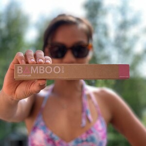 May include: A person holding a brown cardboard box with the text "BAMBOO club toothbrush" printed on it in white and pink.