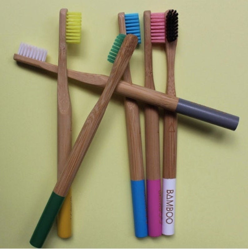 May include: A set of six bamboo toothbrushes with colorful bristles and handles. The handles are painted in different colors, including green, yellow, blue, pink, and white. One handle has the word "BAMBOO" printed on it.