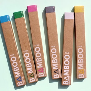 May include: Six cardboard boxes with different colored tops, each containing a bamboo toothbrush. The boxes are labeled "CLUB BAMBOO toothbrush".