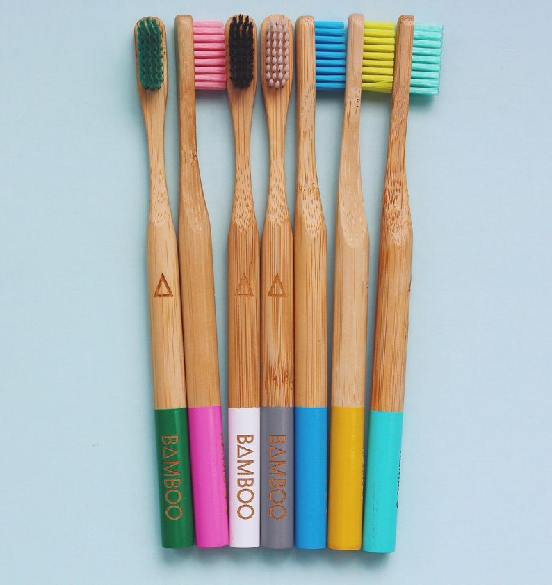 May include: Seven bamboo toothbrushes with colorful bristles and handles. The handles are painted in different colors, including green, pink, white, gray, blue, yellow, and turquoise. The word "BAMBOO" is printed on the handles.