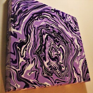 May include: Square canvas art with a swirling abstract design in shades of purple, black, and white. The artwork features a marbled effect, with flowing lines and a textured appearance. The canvas is mounted on a wooden frame.