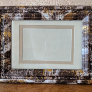 May include: A picture frame with a brown, white, and gold marbled finish. The frame has a double mat and is ready to display a photo or artwork.