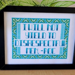 Puede incluir: Arte de punto de cruz enmarcado con la cita "I WILL NOT YIELD TO DISRESPECTFUL MEN. -AOC" en azul y verde. El texto est&aacute; centrado sobre un fondo blanco, enmarcado en negro. El dise&ntilde;o presenta un borde decorativo.