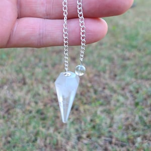 May include: A clear quartz crystal pendulum with a silver chain and a small clear crystal bead at the end of the chain.