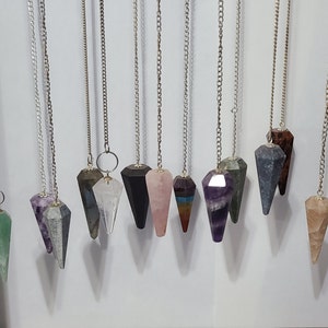 May include: A collection of 12 crystal pendulums with silver chains. The pendulums are made of various crystals, including amethyst, rose quartz, clear quartz, and black obsidian.