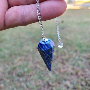 May include: A blue lapis lazuli crystal pendulum with a silver chain and a clear crystal bead at the end.