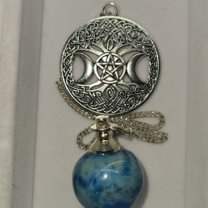 May include: A silver pendant with a tree of life design, three moons, and a pentagram. The pendant is attached to a silver chain with a blue lapis lazuli pendulum.