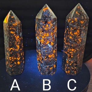 May include: Three hexagonal crystal towers labeled A, B, and C. Each tower features a dark gray base with vibrant, glowing orange and blue inclusions that appear to fluoresce under ultraviolet light, creating a speckled, high-contrast pattern.