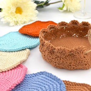 May include: A set of crocheted coasters in various colors, including orange, blue, cream, pink, and light blue, with a larger crocheted basket in a brown color.