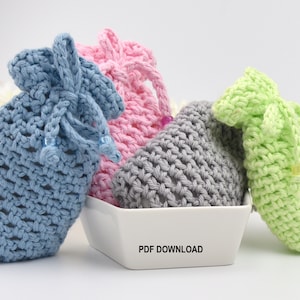 May include: Three crocheted soap saver bags in blue, pink, and green. The bags are sitting in a white ceramic bowl with the words "PDF DOWNLOAD" printed on the bottom.