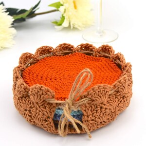 May include: A set of crocheted coasters in orange and brown. The coasters are stacked and tied together with twine.