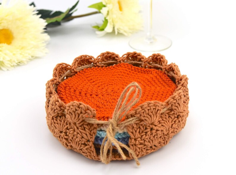 May include: A set of crocheted coasters in orange and brown. The coasters are stacked and tied together with twine.