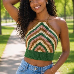 May include: A crochet halter top in a striped pattern of green, pink, brown, and cream. The top is worn with light blue denim jeans. The halter top is a fashionable item of clothing.