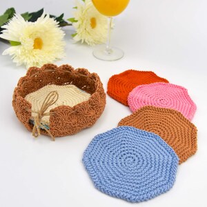 May include: Set of five crocheted coasters in various colors, including orange, pink, brown, and blue. The coasters are arranged in a circle around a crocheted basket.