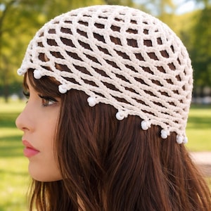 May include: Cream-colored crochet hat with a net-like design. The hat features a rounded shape and is adorned with small, white beads along the edge. The hat is worn on the head.