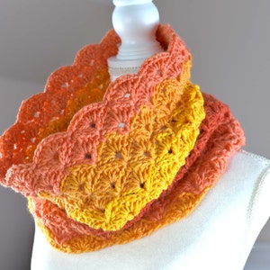 May include: A crocheted infinity scarf in shades of orange, yellow, and red. The scarf is made with a textured stitch and has a scalloped edge.