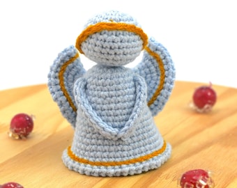 May include: A crocheted angel ornament with blue yarn and a yellow halo. The angel is standing on a wooden surface.