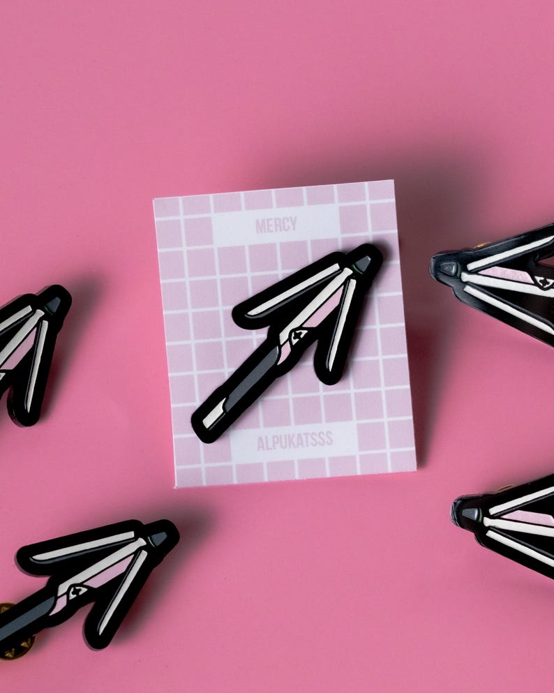 May include: Four black and pink enamel pins shaped like a closed umbrella. The pins are on a pink background. One pin is on a white card with the text "MERCY" and "ALPUKATSSS".