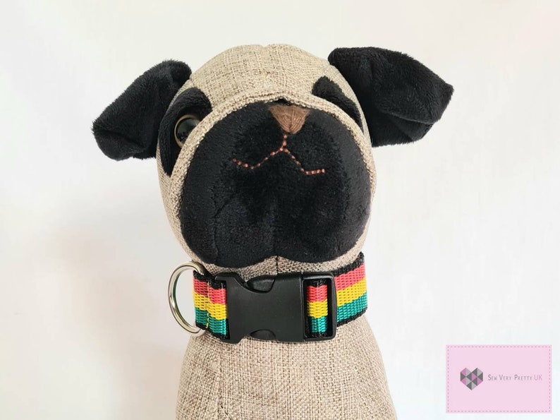 May include: A black and green striped dog collar with a red and yellow stripe. The collar has a black plastic buckle and a silver D-ring.