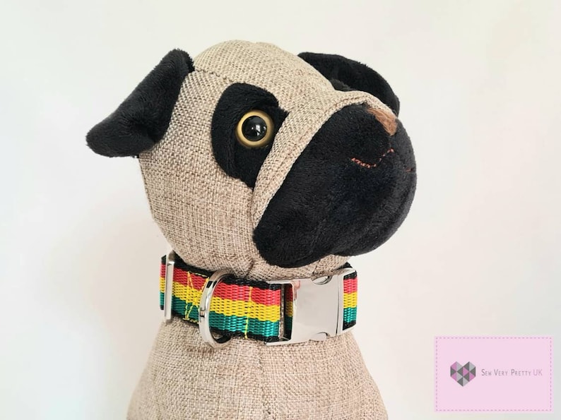 May include: A plush toy pug wearing a colorful dog collar with a silver buckle. The collar has red, yellow, green, and black stripes.