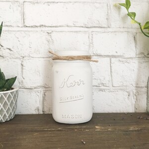 May include: White painted mason jar with a brown twine tied around the lid. The jar has the text "Kerr Self Sealing Mason" embossed on the front.