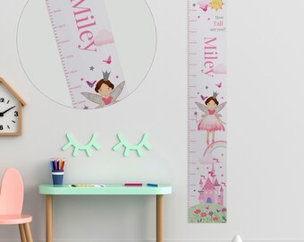 May include: A white and pink personalized growth chart featuring a fairy with a crown and wings. The chart has a rainbow, a castle, and flowers. The text on the chart reads "How Tall are you? Miley".