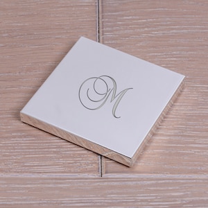 May include: A silver square trinket box with an engraved letter "M" in a cursive font.