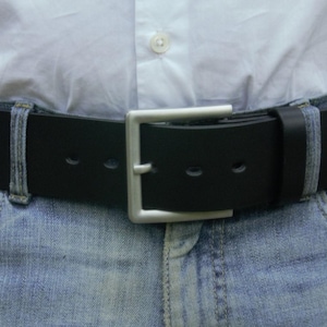 Puede incluir: Un cinturón de cuero negro con una hebilla cuadrada plateada se lleva sobre unos vaqueros azules y una camisa blanca abotonada. El cinturón tiene tres agujeros y un extremo puntiagudo. El cinturón mide aproximadamente 3,8 cm de ancho.