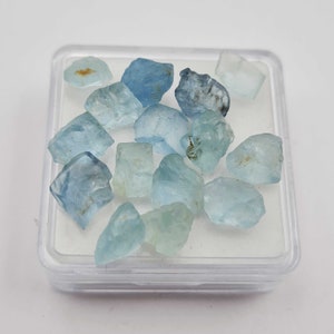 以下が含まれることがあります： 透明なプラスチック容器に入れた、薄い青色のアクアマリンの原石のコレクションです